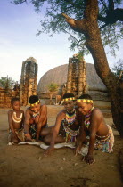 Local children in traditional dress playing a game with stones on the ground outside thatched huts