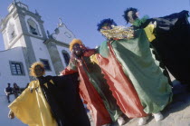 Four Carnival people in bright costume standing in the street outside a church