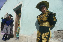 Boy in costume in front of light green house with old woman standing by doorway talking to another boy in costume inside the house