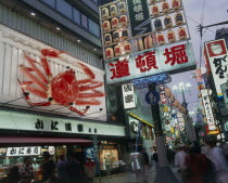 Dotonbori area at night with illuminated sign and buildings and people walking on the pavement