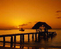 Wooden jet and boat silhouetted at sunset.