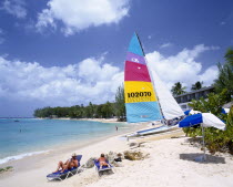 Sandy beach on the West coast fringed with trees and with catamaran and sunbathers.