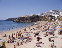 View along the beach from above with sunbathers and the houselined headland beyond