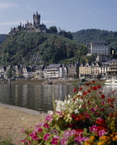 Hilltop castle overlooking houses beside the Mosel River with flowers in the foreground