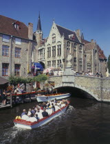 Tourists on boat trips on a canal with old bridge and houses behind