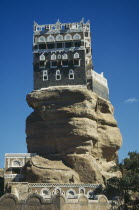 View looking up at grey & white building perched on top of  rock.