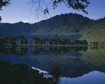 Buttermere.  Rugged hills and trees with mirror reflection in lake.