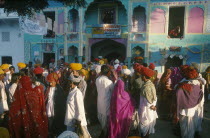 A crowded street of people walking in front of brightly coloured buildings during the Cattle Fair