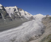 View looking up glacier showing lateral moraine and mountainous sides with a blue sky above