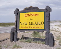 Welcome To New Mexico sign in yellow with a wooden surround beside the road