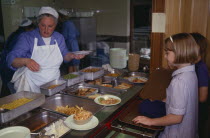 School children with dinner lady serving in the canteen