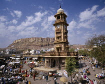 Sadar Market.  Clock tower surrounded by stalls and traders with hillside behind.