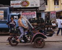 Man riding motorbike laden with beer bottles.  Advertising posters