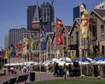 The Rocks harbourside area with people walking past restaurants festooned with umbrellas and flags