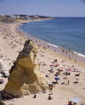 View along the beach from above with a large rock and sunbathers.