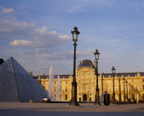 Louvre   Cour Napoleon and glass pyramid in evening light with decorative street lamps and fountain.