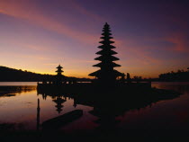 View across Lake Bratan towards island temple of Pura Ulu Danau dedicated to Dewi Danau the goddess of the waters at sunset.