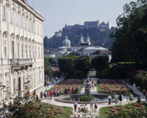 Mirabell Palace with tourists walking in the formal gardens with Hohensalzburg Fortress on the overlooking hill