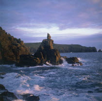 The Irish Lady stone stack below the cliffs with waves crashing against it in the evening light