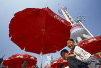 Oriental Pearl communications tower built 1991-1995 and designed by Jia Huan Cheng.  People beneath red parasols with Coca Cola logo in foreground.