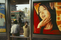 People waiting at bus stop south of Tiananmen Square with advertising hoarding covering exterior wall.Peking Beijing