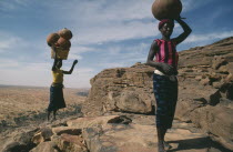 One woman carrying beer and another pots on their heads standing at the top of the Bandiagara Escarpment on their way to village market.