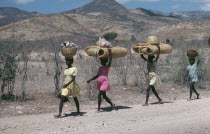 Line of girls carrying bags and baskets on their heads.