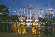 Kachin Manou Dance leaders passing Manou posts in the background