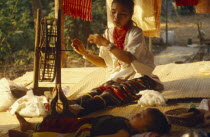 Lawa woman spinning thread inside her house with her young son lying in the foreground