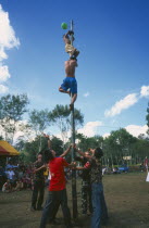 Kachin Manou. Kachin boy reaches the prize climbing a greased bamboo pole