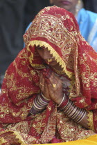 Sankat Mochan Mandir temple. Hindu bride dressed in red and gold sari with her hands in namaste gesture painted with henna design and wearing glass bracelets