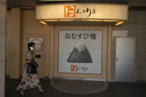 Onigiri rice ball shop sign in front of Tokyo Station with passing woman using cell phone