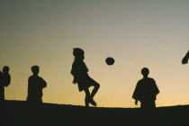 Hilltribe kids playing football with a coconut silhouetted against evening sky.