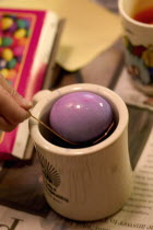 Child dipping Easter egg into a mug of purple dye.