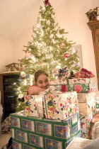 Girl aged 12 happily surronded by piles of Christmas presents and decorated tree behindCentre