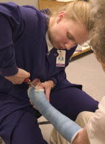 Clinic nurse making adjustments to cast with cutter for elderly patient with a broken wristAges 28 and 90.