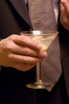 Business man holding martini cocktail at social gathering.