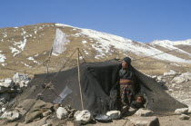 Tibetan nomad woman and child looking out of tent made of yak wool on winter pasture land.