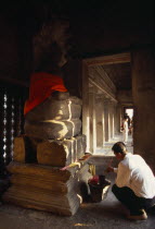 Interior of shrine on the upper level with visitor lighting incense at base of Buddha figure seated below naga with multi headed hood.Asian Bonnet Cambodian Kampuchea Religion Southeast Asia History...