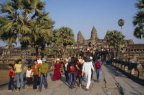 Tourists on tree lined stone causeway leading to temple complex.  Many Cambodians visiting during Chinese New Year. Asian Kampuchea Religion Southeast Asia History Holidaymakers Kamphuchea Religious...