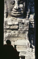 Bayon Temple with a monk sitting in a doorway in front of one of the four faced towersAsian Cambodian Kampuchea Religion Southeast Asia 1 4 History Kamphuchea Religious Single unitary One individual...