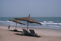 Hotel beach front with woman and child walking hand in hand over sand. Sun loungers and parasols in the foreground