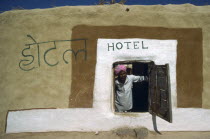 Man in turban looking out of low open doorway of village hotel.