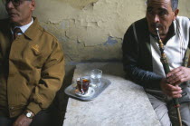 Two men in street cafe one drinking tea and one smoking a sheesha waterpipe.