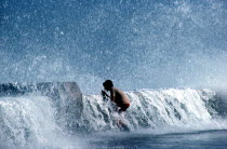 Young boy standing on pavement with waves crashing over the sea wall