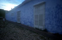 House with blue walls in cobbled street with a woman in white walking past