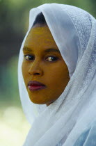 Portrait of young woman in white head covering with face stained with yellow powder.