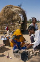 Couple lighting a fire inside stone surround on sandy ground outside their nomadic shelter