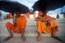 Two young monks seated on wide stone steps under umbrellas.