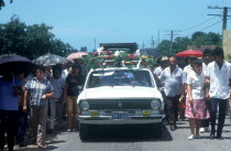 Funeral procession with car carrying flowers and coffin on its roof